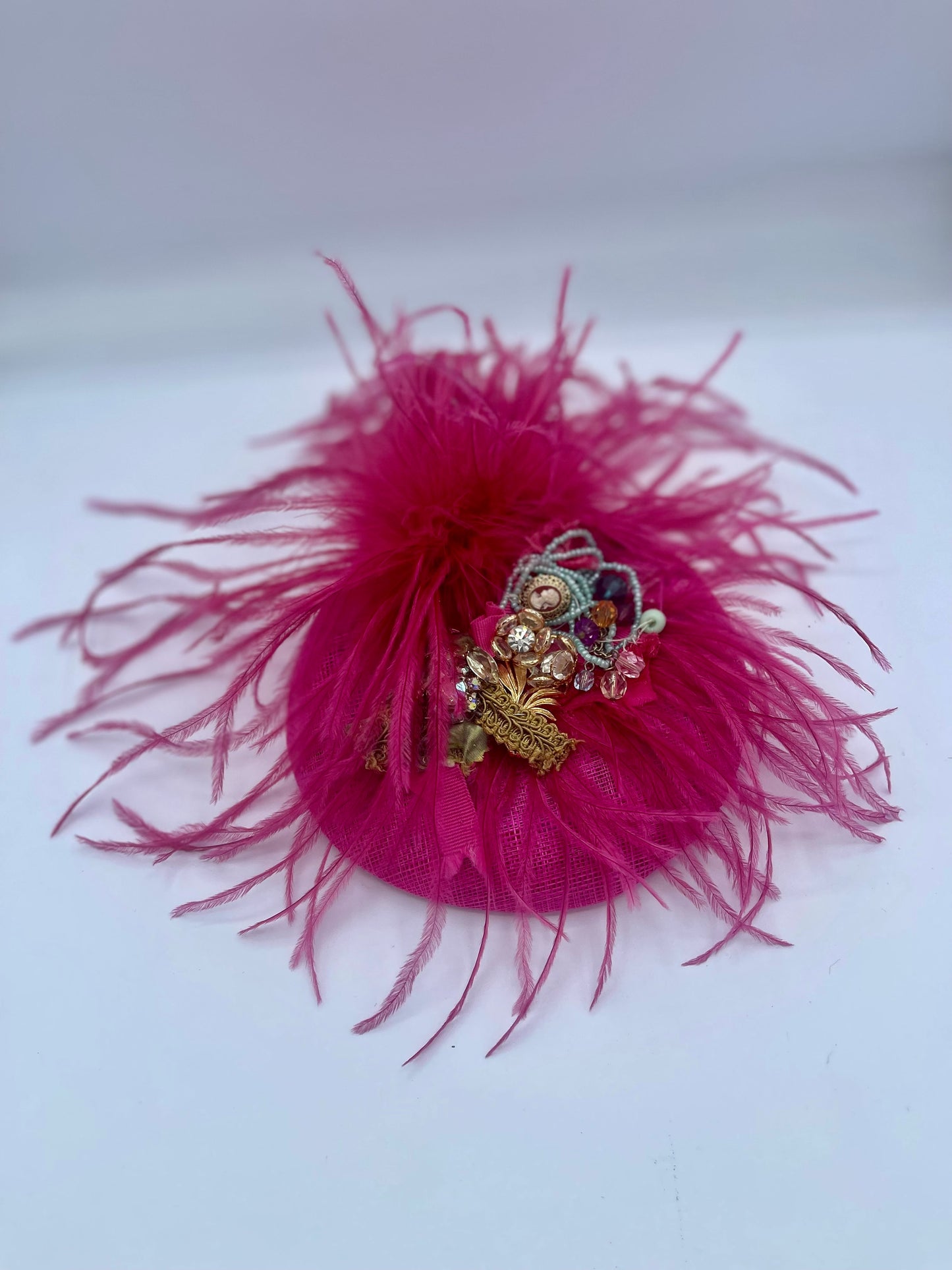 Magenta colored fascinator with feathers and bejeweled center